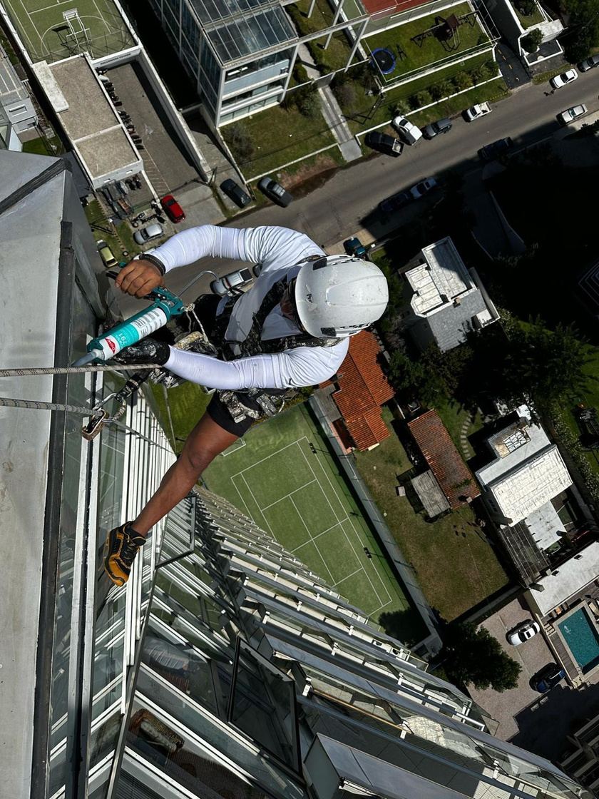 Operario en cuerda aplicando sellador en una baranda de vidrio, sobre una cancha de tenis